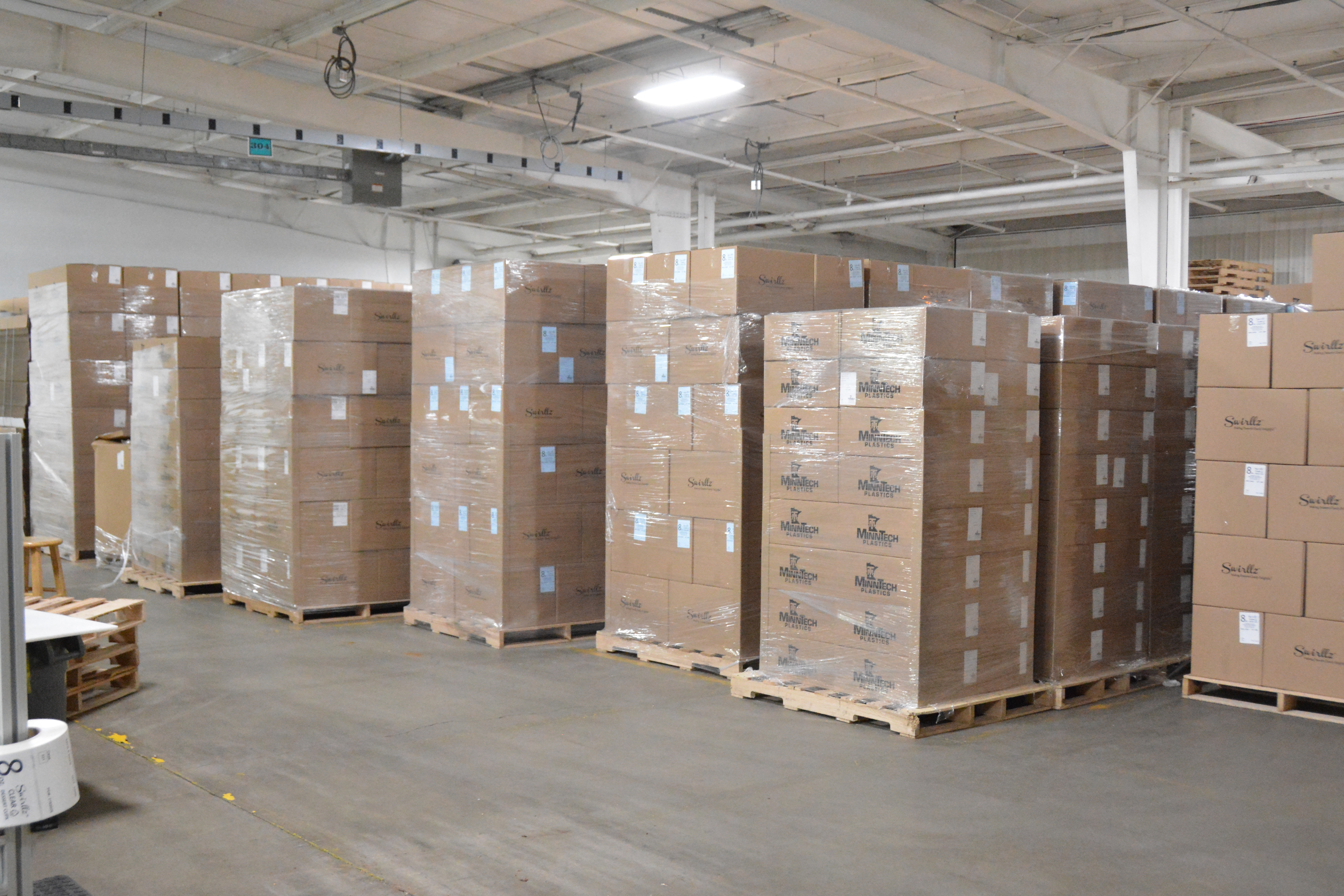 MinnTech Plastics warehouse with rows of stretch wrapped pallets of MinnTech branded and Swirlz corrugated cases staged on wooden pallets for distribution