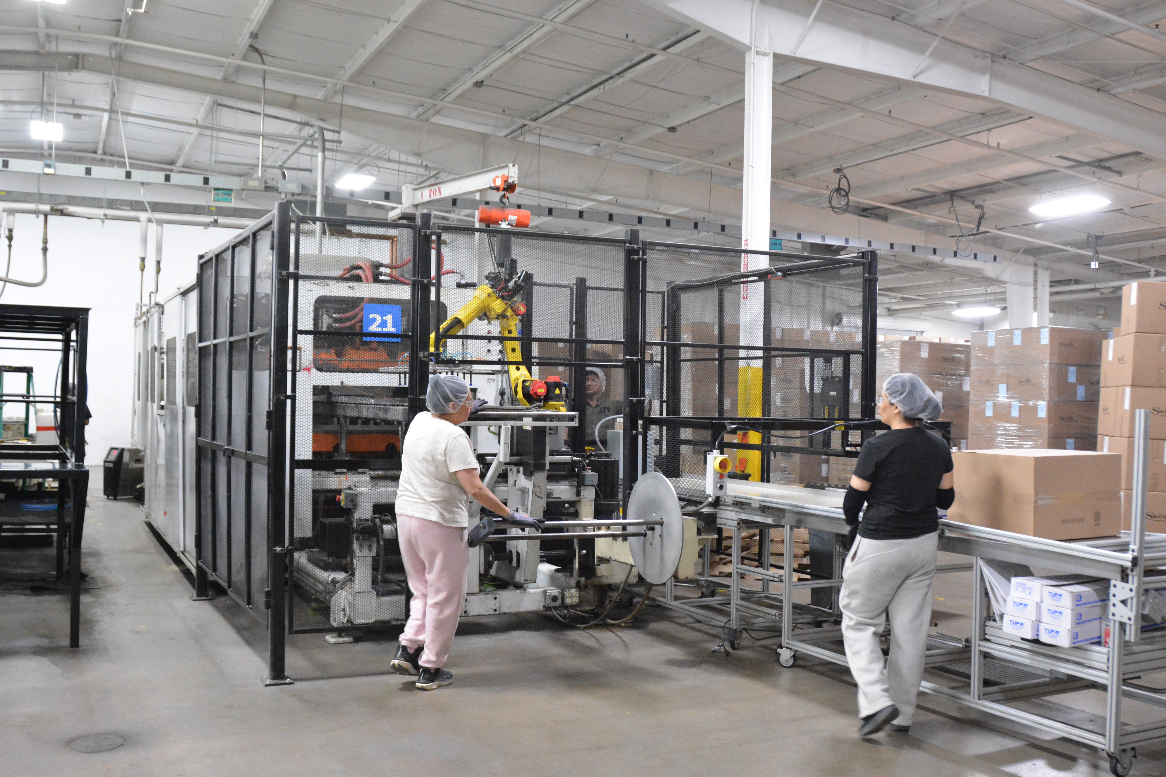 Two MinnTech Plastics production workers operating a safety guarded robotic thermoforming cell with FANUC arm and case packing station